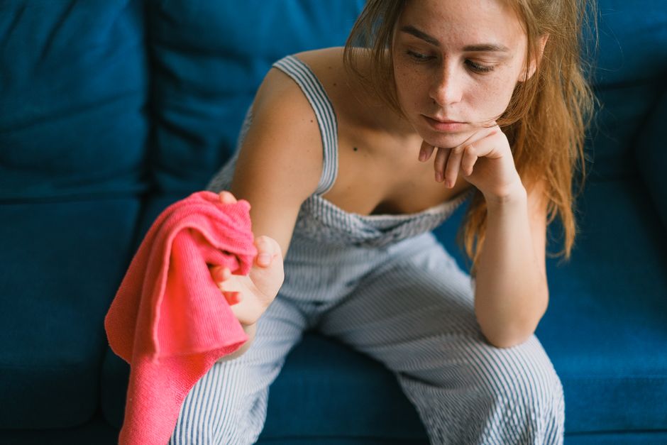 A household living room featuring a blue fabric sofa with a cream-colored throw draped over the armrest, situated against a plain light gray wall. Adjacent to the sofa, there is a round, reflective me