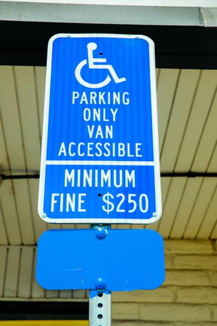 A blue and white parking sign indicating parking for van access only with a wheelchair symbol, displaying a minimum fine of $250. The sign is mounted on a metal pole beneath a ceiling structure, likel